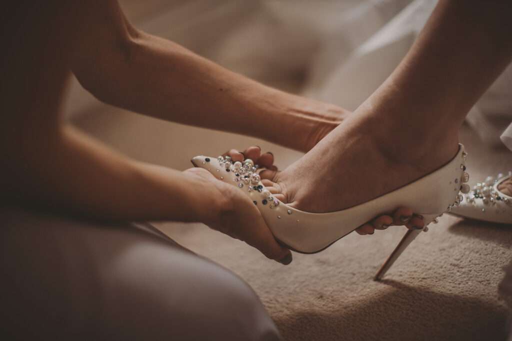 bride being helped into wedding shoes