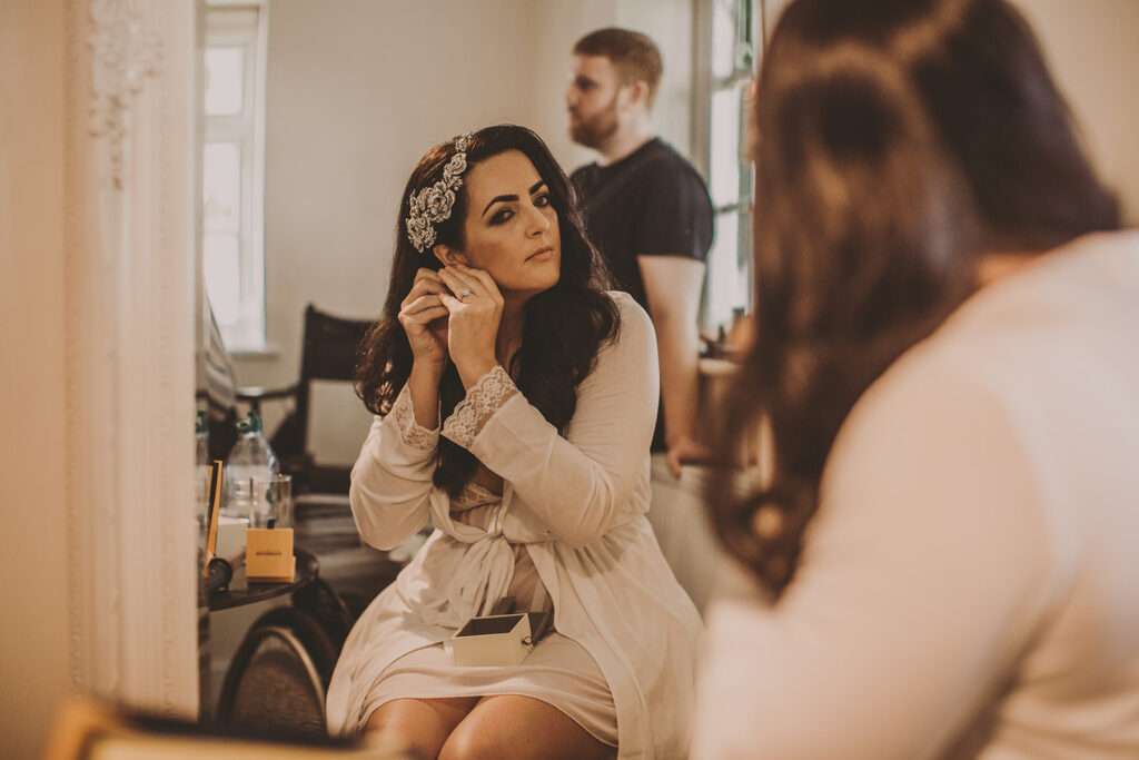 bride puts in her earrings as bridesmaids get ready at Colshaw Hall