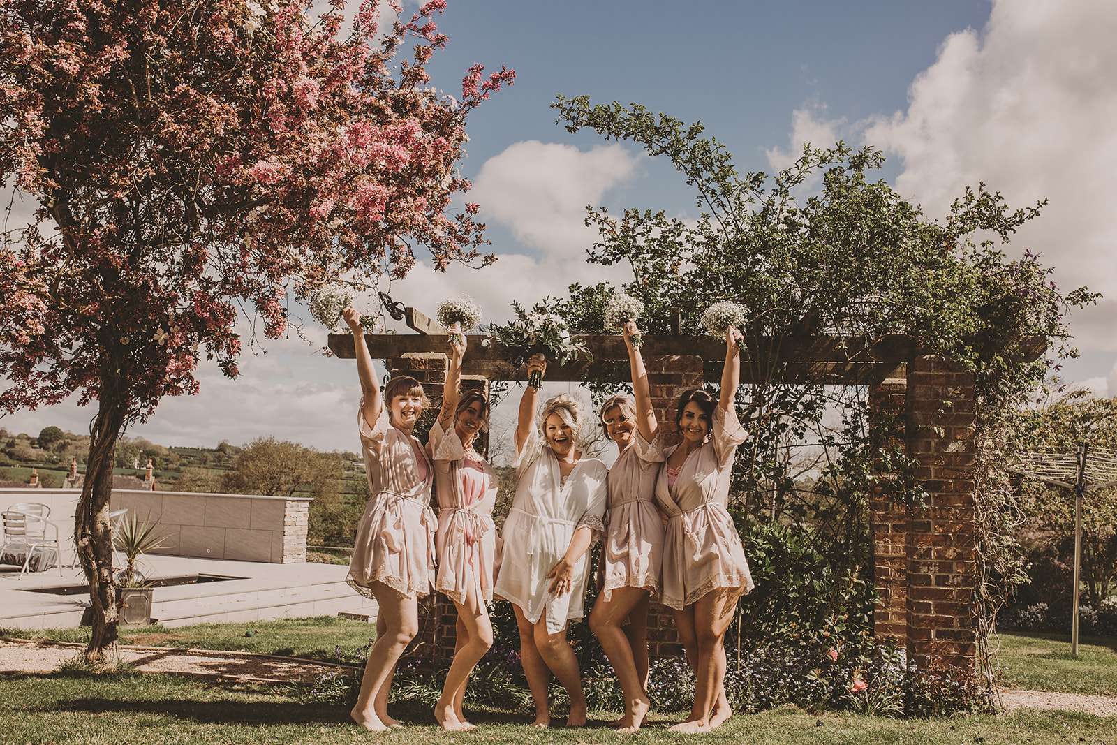 bride and bridesmaids holding flowers in the air in the gardens at Osmaston Hall