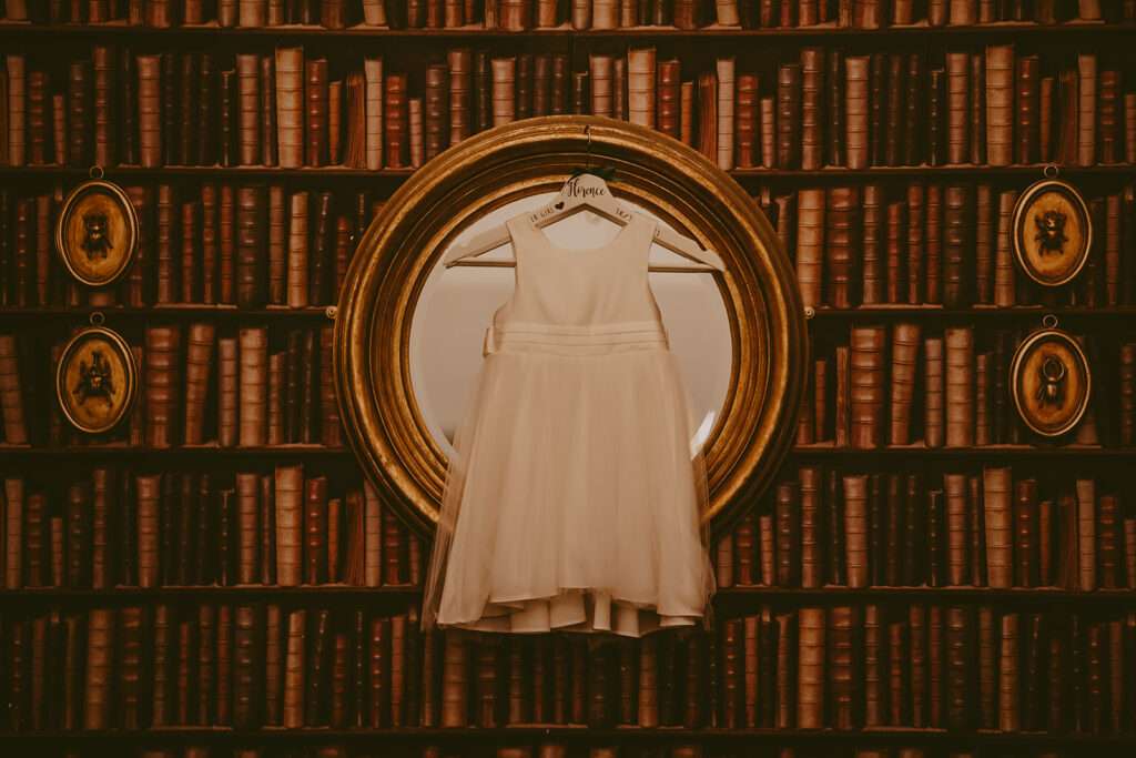 white flower girls' dress hanging on mirror